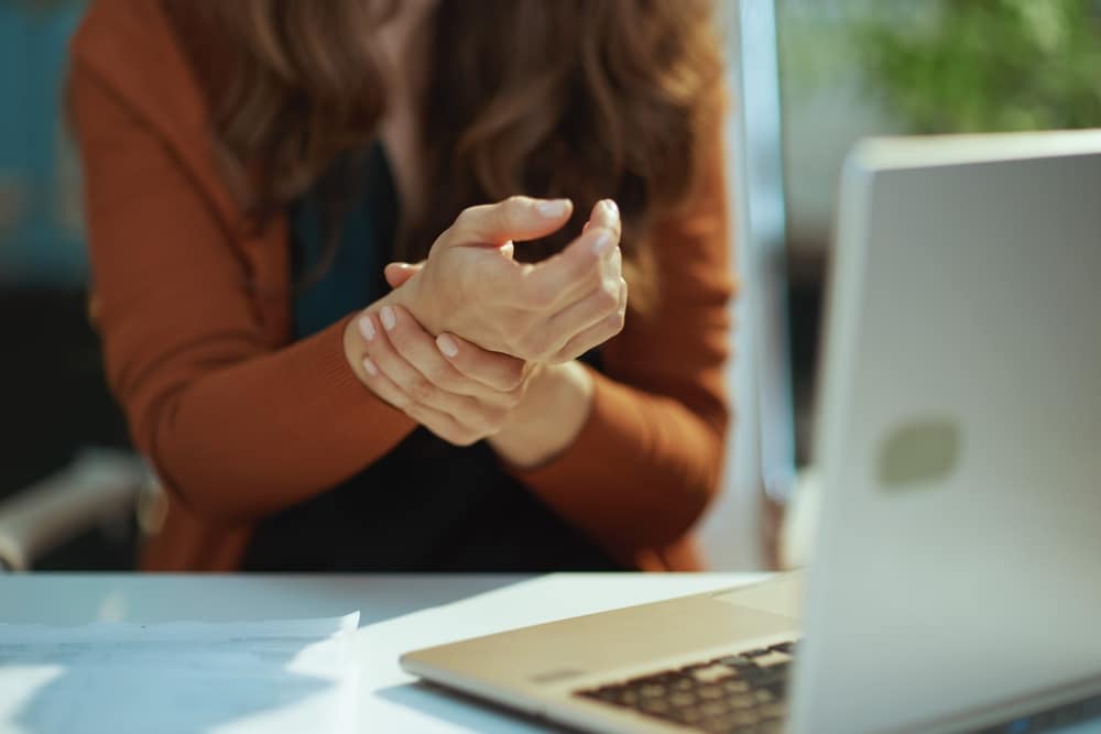 A woman typing on a laptop and struggling with carpal tunnel syndrome, in need of nerve decompression for pain relief.